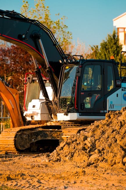 Excavator beside large piles of excavated soil on a property during pond work