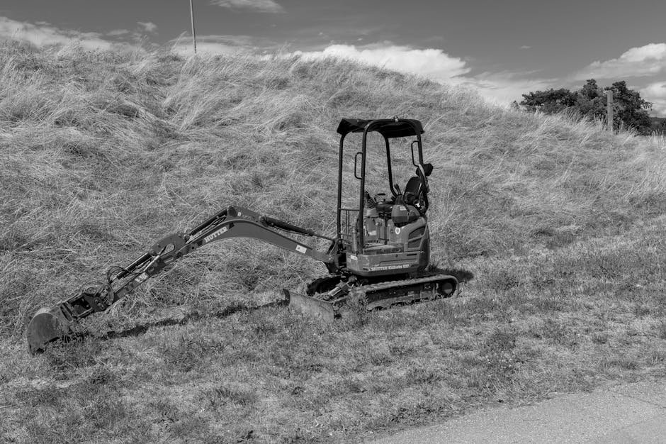 Mini ekskavatorius dirba siauroje tranšėjoje šalia namo kieme