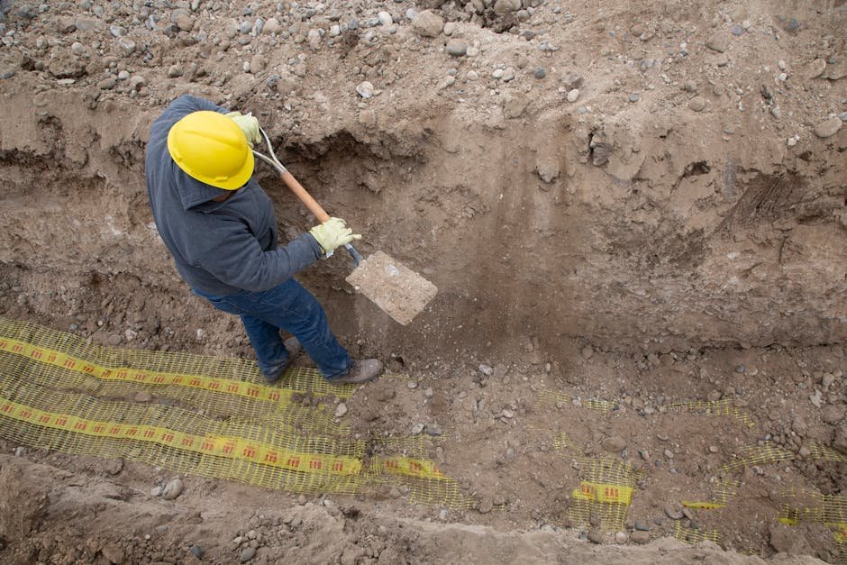 Drainage trench with gravel and fabric being installed beside a sloped ground area
