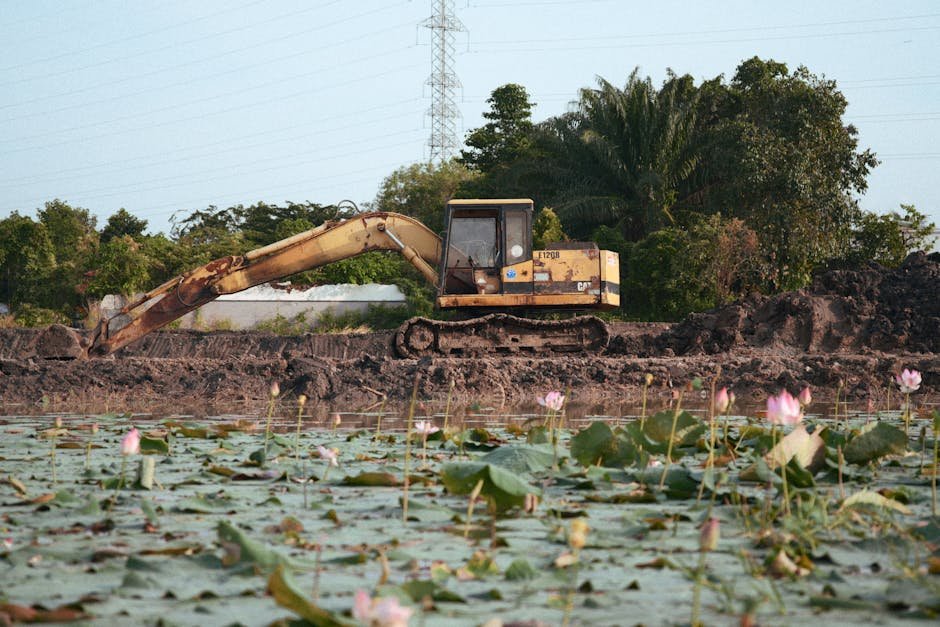 Large excavator digging a pond in an open field with piles of soil nearby