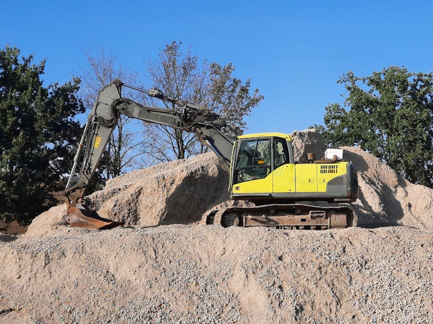 Excavator and skid steer working on a gravel driveway base near a house