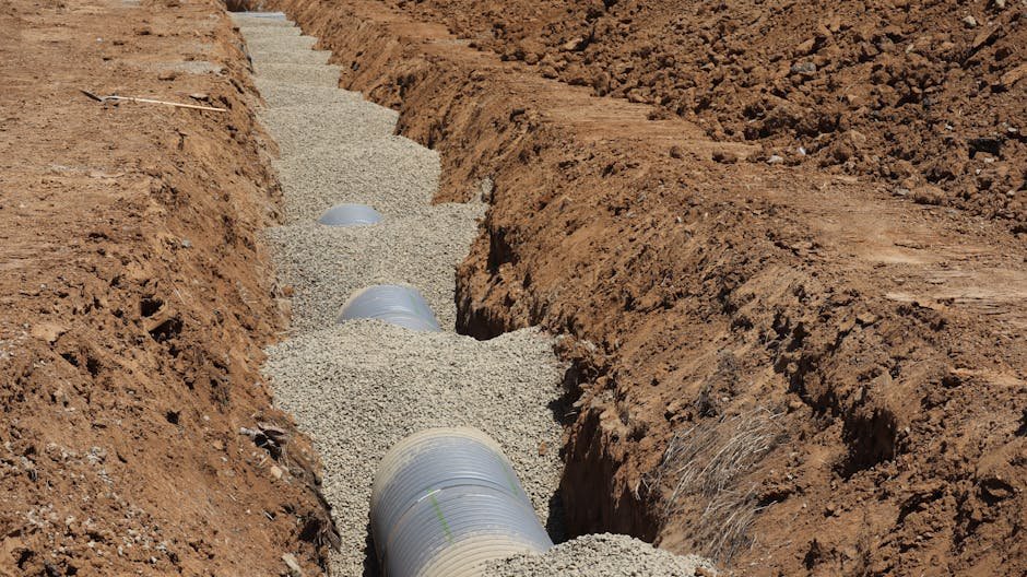 Excavator digging a trench for drainage or utility lines in a dry yard
