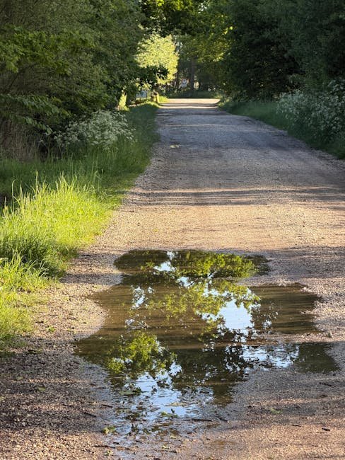 Rural gravel driveway with puddles and soft sections after heavy rain